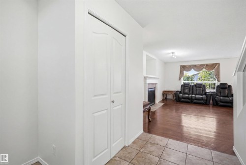 Entryway featuring ceramic tile flooring, leading to a living area with wood-finish flooring, a white mantel fireplace, and a large window with exterior greenery - 1560 37B Avenue, Edmonton, AB 