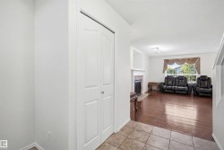 Entryway featuring ceramic tile flooring, leading to a living area with wood-finish flooring, a white mantel fireplace, and a large window with exterior greenery - 