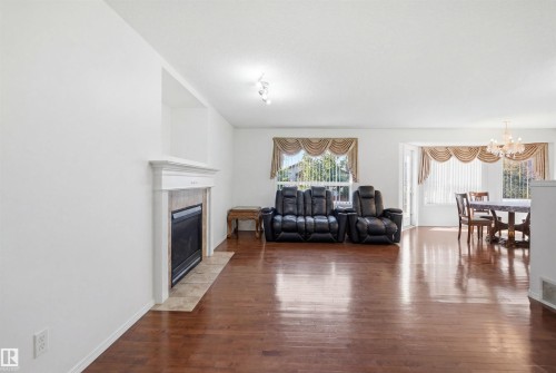 Spacious interior with wood-finish flooring, a fireplace featuring a tile surround and white mantel, and ample natural light from multiple windows - 1560 37B Avenue, Edmonton, AB 