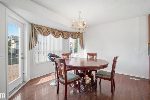 Dining area featuring wood-finish flooring, a bay window with vertical blinds and draped valance, a frosted glass chandelier, and a glass-paneled exterior door opening to a deck - 1560 37B Avenue, Edmonton, AB 