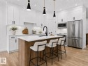 Modern kitchen featuring white shaker cabinetry with matte black hardware, a wood-finish island with seating, stainless steel appliances, and wood-finish flooring - 3318 Chickadee Drive, Edmonton, AB 