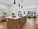 Open-concept living area featuring a kitchen island with stone countertop, black sink, and modern pendant lighting - 3318 Chickadee Drive, Edmonton, AB 