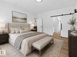 Bedroom with light wood-finish flooring, white walls, and a white barn door - 
