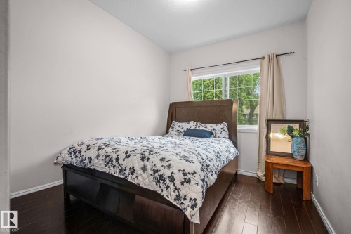 Bedroom featuring dark wood-finish flooring, a large window with white trim, and light-toned walls - 4806 117 Ave, Edmonton, AB 