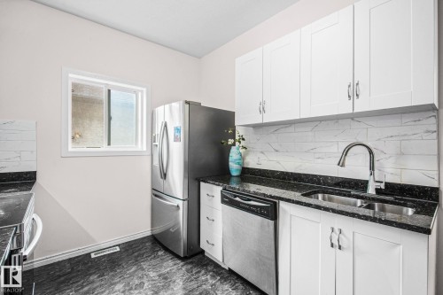 Kitchen featuring white upper cabinetry, stainless steel appliances, dark speckled countertops, and a white subway tile backsplash - 4806 117 Ave, Edmonton, AB 