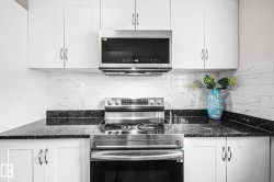 Modern kitchen featuring a stainless steel range with overhead microwave, white cabinetry with silver hardware, black speckled countertops, and a white subway tile backsplash - 