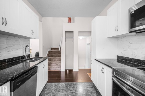 Contemporary kitchen featuring white cabinetry, dark speckled countertops, a stainless steel sink with a gooseneck faucet, a stainless steel dishwasher, and a white and gray tiled backsplash - 4806 117 Ave, Edmonton, AB 