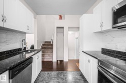 Contemporary kitchen featuring white cabinetry, dark speckled countertops, a stainless steel sink with a gooseneck faucet, a stainless steel dishwasher, and a white and gray tiled backsplash - 