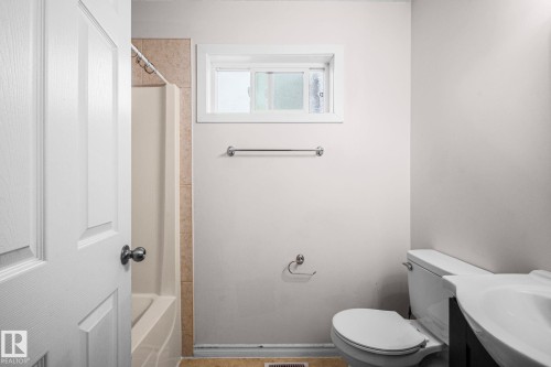 Bathroom featuring a white bathtub with a tiled surround, a window with white trim, and a commode - 4806 117 Ave, Edmonton, AB 