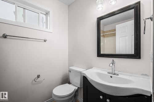 Bathroom featuring a dark wood-finish vanity with an integrated white sink, a framed mirror, and chrome fixtures - 4806 117 Ave, Edmonton, AB 