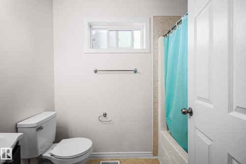 Bathroom featuring a white toilet, an acrylic bathtub with a tiled surround, a white framed window, and a paneled interior door with a dark knob - 4806 117 Ave, Edmonton, AB 