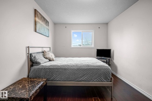 Bedroom featuring a window with natural light, dark wood-finish flooring, and white baseboards - 4806 117 Ave, Edmonton, AB 
