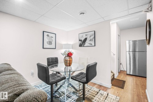 Compact dining area featuring a glass-top table, four counter-height chairs, and wood-finish flooring - 4806 117 Ave, Edmonton, AB 