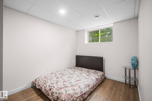 Bedroom featuring wood-finish flooring, a drop ceiling with recessed lighting, and a window providing natural illumination - 4806 117 Ave, Edmonton, AB 