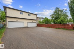 Cream-colored siding building featuring two ground-level garage doors, upper-level windows, and a dark trim - 