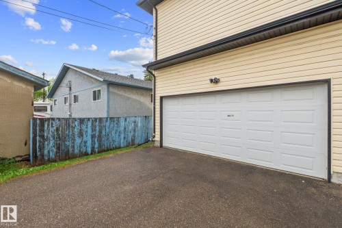 Attached garage featuring a white panel door, light-colored horizontal siding, dark gutters, and exterior lighting - 4806 117 Ave, Edmonton, AB 