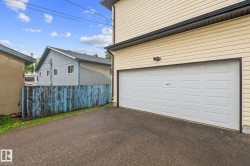 Attached garage featuring a white panel door, light-colored horizontal siding, dark gutters, and exterior lighting - 