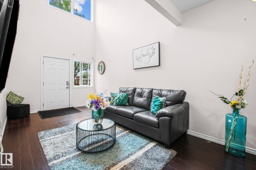 Living room featuring wood-finish flooring, a white paneled entry door, and large transom windows - 4806 117 Ave, Edmonton, AB 