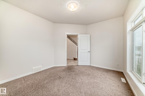 Carpeted room with white walls, a large window, a white interior door, and a flush-mount ceiling light fixture - 18103 77 Street, Edmonton, AB 