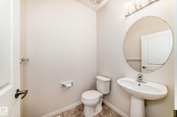 Pedestal sink with a circular mirror, brushed nickel light fixture, toilet, and tile flooring - 