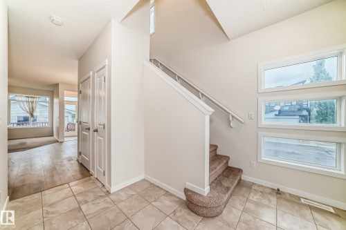 Entryway featuring tile flooring, a carpeted staircase with white railings, and three horizontal windows providing natural light - 18103 77 Street, Edmonton, AB 
