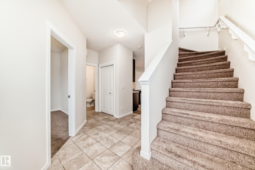Carpeted staircase with white balusters, leading up from a tiled entryway - 18103 77 Street, Edmonton, AB 
