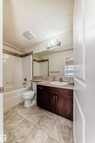 Bathroom featuring a wood-finish vanity with an integrated sink, a large wall mirror, and a three-light fixture - 18103 77 Street, Edmonton, AB 