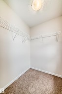 Walk-in closet featuring built-in wire shelving, neutral carpeting, white baseboards, and a flush-mount ceiling light - 