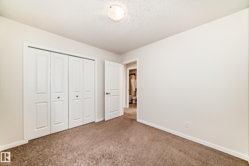 Carpeted room featuring white bi-fold closet doors, a white interior door, and a flush mount ceiling light - 18103 77 Street, Edmonton, AB 