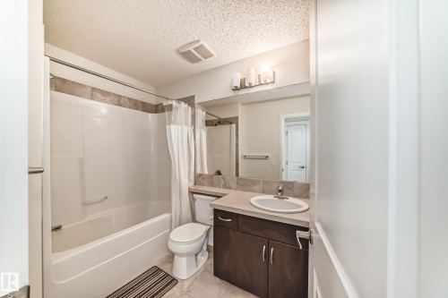 Bathroom featuring a combined tub and shower with tile surround, a dark wood-finish vanity with an integrated sink and light-toned countertop, and an overhead vanity light fixture - 18103 77 Street, Edmonton, AB 