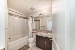 Bathroom featuring a combined tub and shower with tile surround, a dark wood-finish vanity with an integrated sink and light-toned countertop, and an overhead vanity light fixture - 