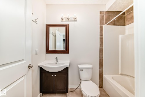 Bathroom featuring a white vanity with integrated sink, dark wood-finish cabinet, and a framed mirror - 18103 77 Street, Edmonton, AB 