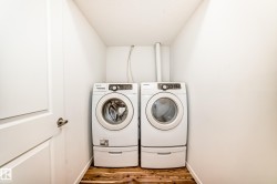 Dedicated laundry area featuring a front-loading washer and dryer set with pedestal bases, wood-finish flooring, and crisp white walls - 