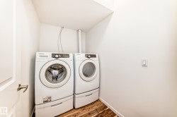 Dedicated laundry area featuring wood-finish flooring, white walls, and a light switch with a white cover plate - 