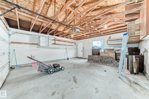 Spacious garage with exposed wood ceiling beams, concrete flooring, and an overhead garage door - 18103 77 Street, Edmonton, AB 