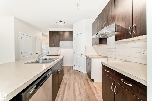 Kitchen featuring wood-finish flooring, dark wood cabinetry, light-toned countertops, and a subway tile backsplash - 18103 77 Street, Edmonton, AB 