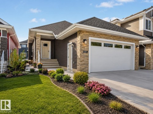 Stone veneer and horizontal siding exterior featuring a prominent two-car garage with transom windows - 3320 Chickadee Drive, Edmonton, AB 