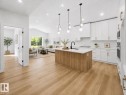 Open-concept living space featuring a kitchen island with wood-finish paneling, white shaker-style cabinetry, and light wood-finish flooring throughout - 3320 Chickadee Drive, Edmonton, AB 