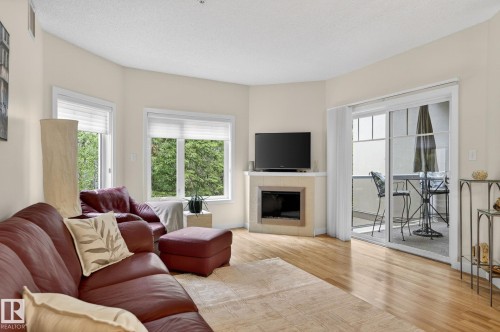 Living area featuring wood-finish flooring, a corner fireplace with tile surround, and multiple windows - 208 5 Gate Avenue, St. Albert, AB 