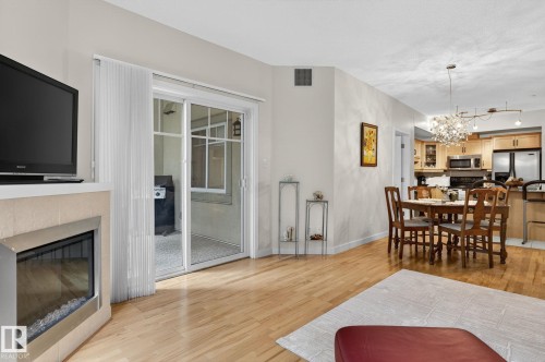 Open-concept living space featuring wood-finish flooring, a contemporary fireplace with a stone surround, and direct access to a screened-in patio - 208 5 Gate Avenue, St. Albert, AB 