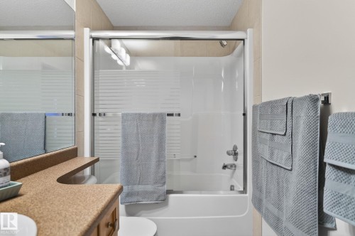 White bathtub with a sliding glass shower door and integrated shower fixtures - 208 5 Gate Avenue, St. Albert, AB 