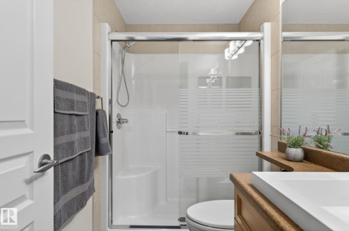 Enclosed shower with frosted glass door, light-toned wall tiling, built-in shower bench, and polished chrome fixtures - 208 5 Gate Avenue, St. Albert, AB 