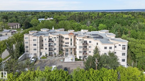 Multi-story condominium building featuring a light-toned facade, multiple private balconies, a central covered entrance, and an integrated parking area - 208 5 Gate Avenue, St. Albert, AB 