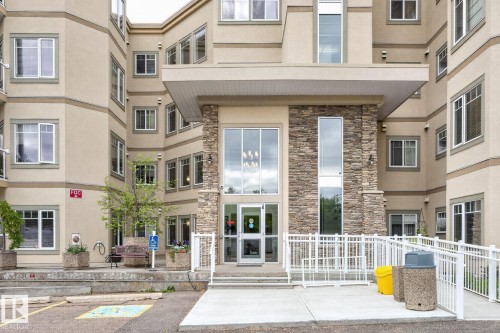 Multi-story building featuring a stone-clad entrance with large glass doors and windows, a covered entryway, and a concrete accessibility ramp with white railings - 208 5 Gate Avenue, St. Albert, AB 