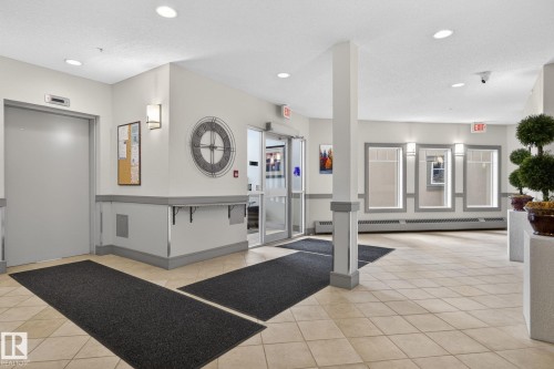Common area featuring neutral wall tones with grey trim, recessed lighting, wall sconces, large format tile flooring, and a glass-paneled entrance - 208 5 Gate Avenue, St. Albert, AB 