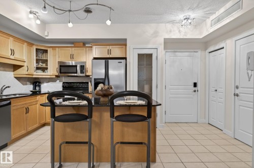 Kitchen featuring light wood cabinetry, stainless steel appliances, a black countertop island with seating, a white tile backsplash, and ceramic tile flooring - 208 5 Gate Avenue, St. Albert, AB 