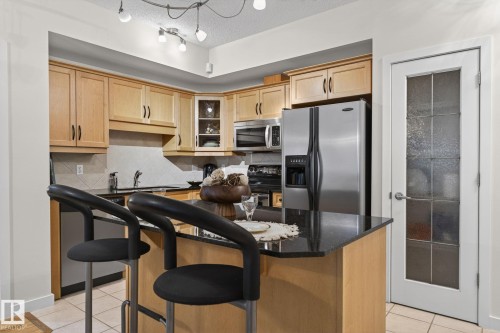 Kitchen featuring light wood cabinetry, a granite-finish island, and stainless steel appliances - 208 5 Gate Avenue, St. Albert, AB 