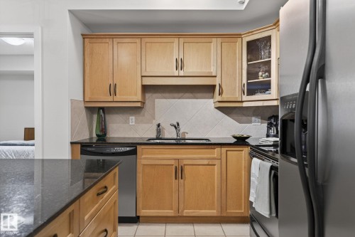 Kitchen featuring natural wood cabinetry, dark countertops, stainless steel appliances, tile flooring, and a tile backsplash - 208 5 Gate Avenue, St. Albert, AB 