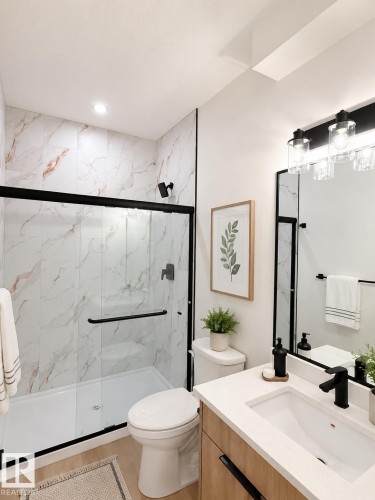 Bathroom featuring a glass-enclosed shower with black trim, marble-patterned wall tiling, and a white shower pan - 3150 Magpie Way, Edmonton, AB 