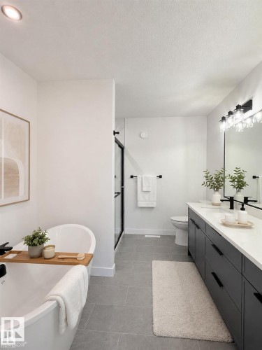 Contemporary bathroom featuring a freestanding soaking tub, a dual-sink vanity with dark cabinetry, a glass-enclosed shower, a wall-mounted light fixture, and grey floor tiles - 3150 Magpie Way, Edmonton, AB 